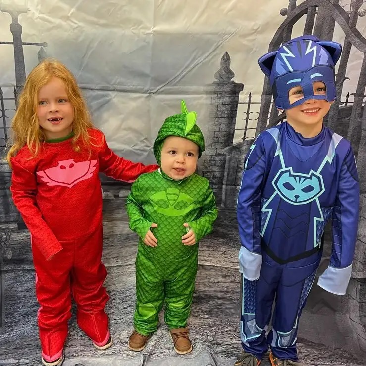 Three children in superhero Halloween costumes posing at a Howl-o-Ween photo booth in Carol Stream