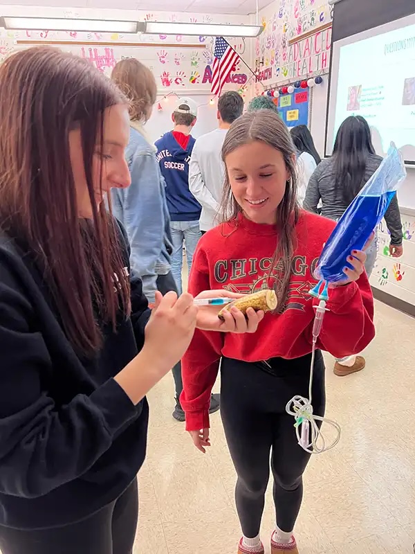 High school students examining veterinary IV equipment during a hands-on education presentation in Carol Stream