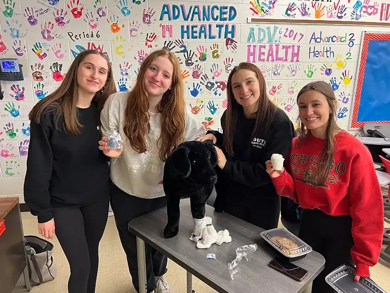 Students posing with a stuffed dog and veterinary supplies during a school education event in Carol Stream