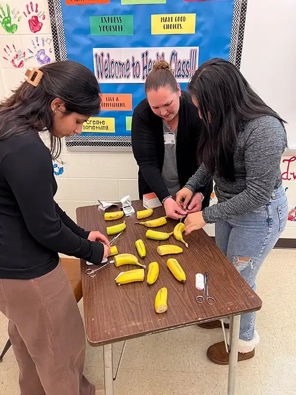 Veterinary staff demonstrating suturing techniques on bananas with students in a health class in Carol Stream